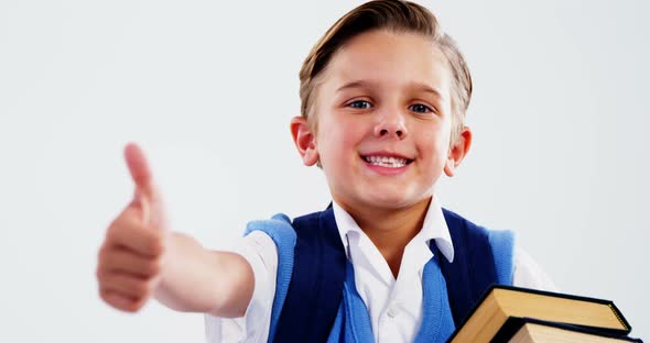 Smiling schoolboy with books showing thumbs up