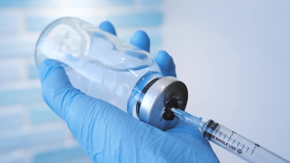 A Doctor or Nurse in Blue Medical Gloves Dials Medicine Into a Syringe