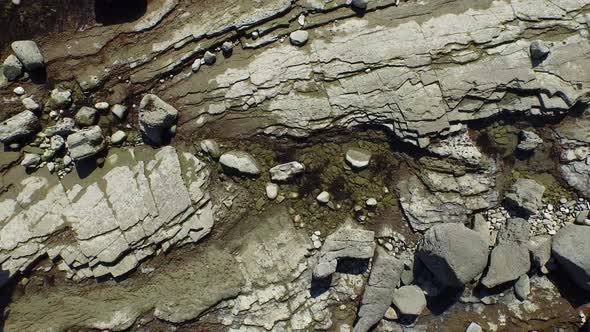 Aerial shot of young man running on a scenic rocky beach coastline.