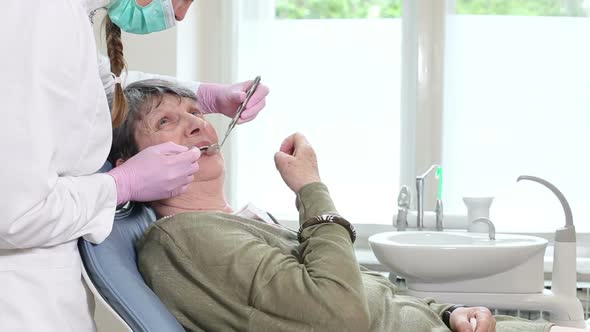 Elderly woman showing aching tooth to female dentist