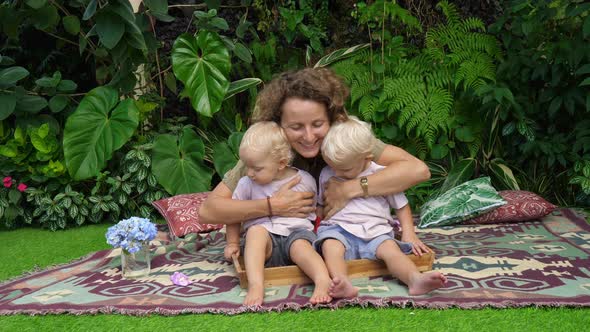 Young White Mom Cuddling Her Toddler Twins While Picnicing in the Park