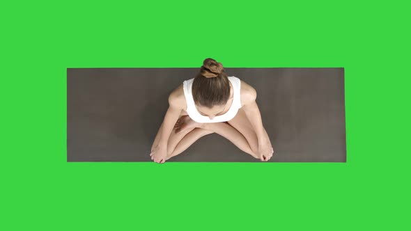 Young Sporty Woman Practicing Yoga Sitting in Lotus Pose and Breathing Deeply on a Green Screen