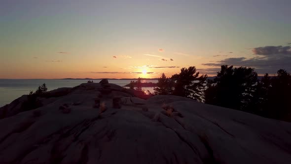 Reveal of Inukshuk on Rocky Pine Tree Island at Sunset, Drone Aerial Wide Dolly Out. View of Blue La