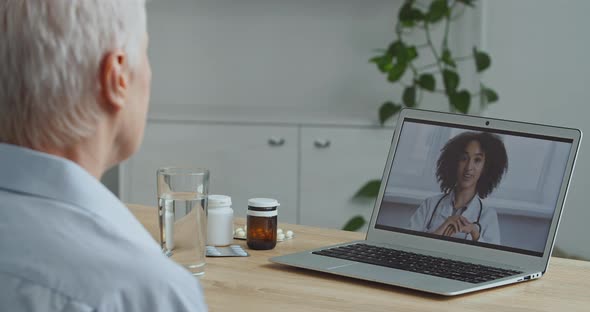 View From Behind Aging Sick Woman Patient Grandmother Makes Video Call on Laptop To Doctor Speaks To