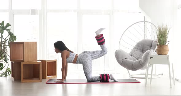 Pretty fitness black woman in sportswear practicing donkey kick exercise with ankle weight.