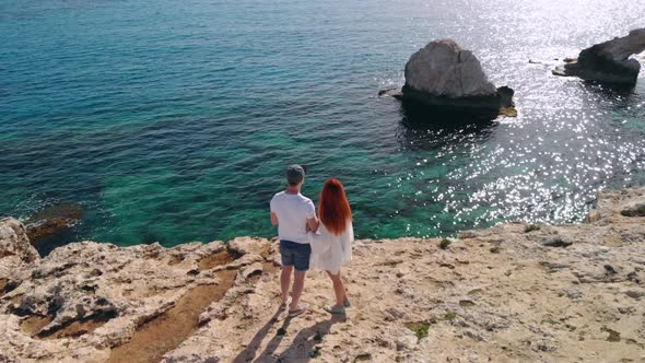 Aerial View of Couple Standing on Edge of Cliff By Sea