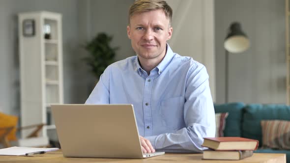 Smiling Businessman Looking at Camera While Working on Laptop