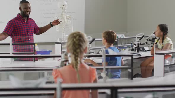 Video of happy african american teacher with class of diverse pupils during anatomy lesson