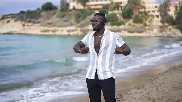 Portrait of Happy Relaxed Male African American Tourist in Headphones Dancing on Sandy Beach