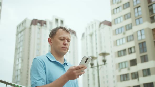 Citizen Surfs in His Mobile Phone Writes a Text Message Stands Background of City Buildings