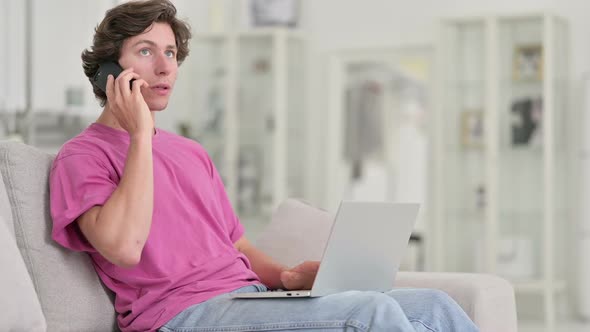 Young Casual Man with Laptop Talking on Smartphone at Home