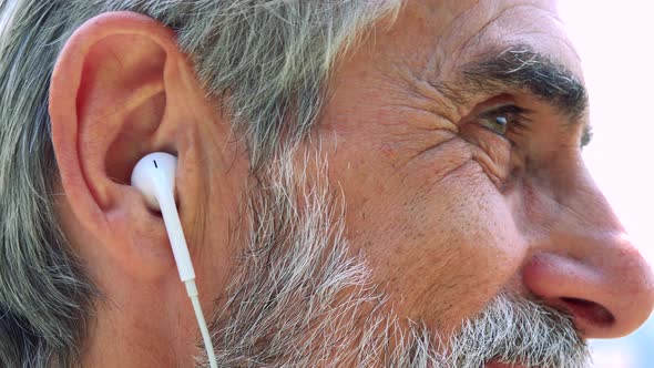 Old Senior Man Listens Music with Earphone on Smartphone - Closeup