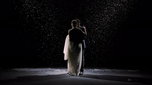 A Charming Couple in Love Dances Against the Background of Falling Snow. A Man in a Suit and a Woman