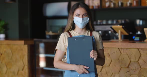 Beautiful Woman Barista Standing Next to the Barlooking at Camera and Taking Off Protective Mask