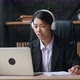 Asian Woman in Headphones Using Laptop for Distance Learning and Writes Notes While Sitting at Home - VideoHive Item for Sale