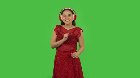 Tender Girl in Red Dress Is Dancing and Enjoying Music in Big Red Headphones. Green Screen