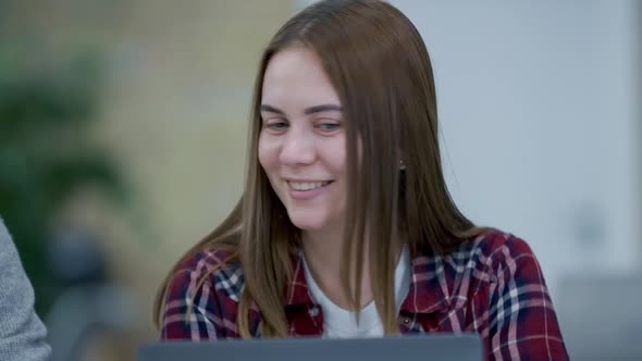 Close-up Portrait of Beautiful Young Caucasian Woman Sitting in Office with Laptop and Talking To