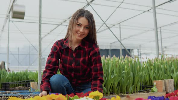 Joyful Young Female Florist with a Smile Sitting Near Colorful Flowers