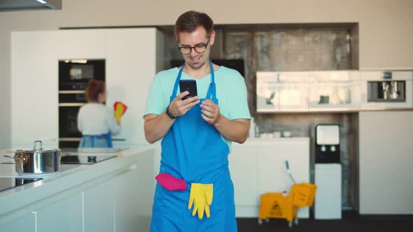 Male Professional Cleaner Using Smartphone Standing in Modern Home Kitchen