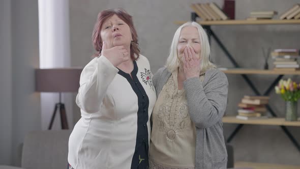 Medium Shot of Two Joyful Senior Women Sending Air Kiss at Camera Hugging Smiling