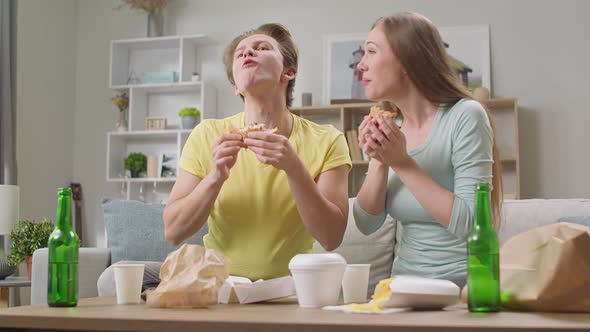 Young Couple Eating a Hamburger and Watching TV in the Living Room