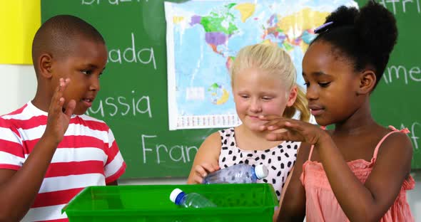 School kids putting waste bottle on recycle logo box in classroom