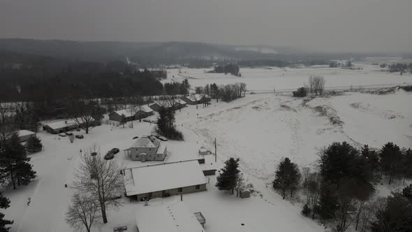 Aerial view of rural neighborhood in snow covered valley.  Cloudy sky and mountains in distance. alt