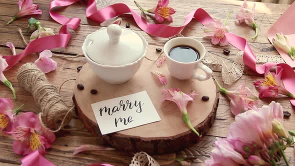 MARRY ME card near coffee and flowers on a wooden table