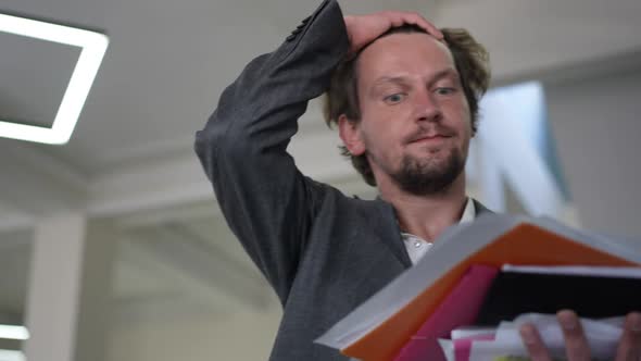 Portrait of Concentrated Male Analyst Adjusting Hair Shaking Head Looking Through Documents Indoors