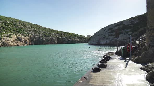 Turquoise Magrr Ix-Xini Bay Sea Water Washes Stone Pier Filled with Rubber Tires