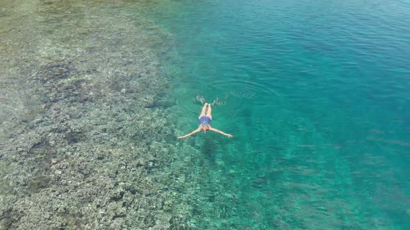 Aerial: woman snorkeling on Pulau Gunung Api coastline coral reef tropical