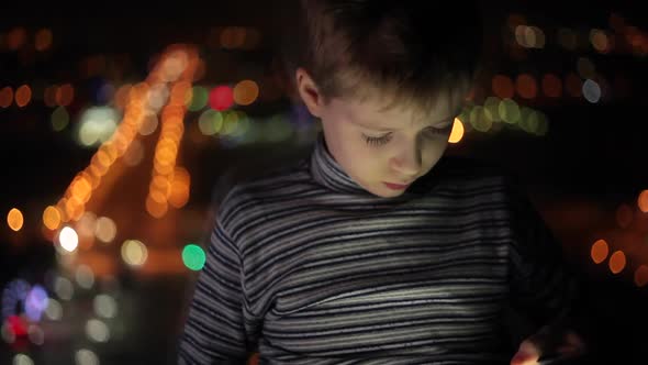 Young Boy Plays with the Tablet in the Evening