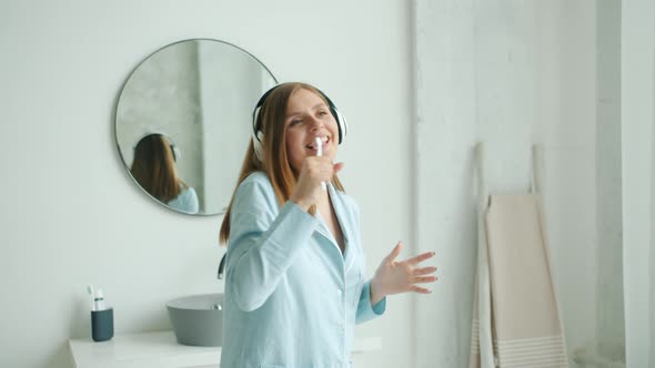 Cheerful Girl in Headphones Brushing Teeth Singing Dancing in Bathroom at Home