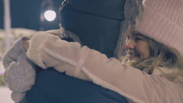 Young Woman Hugs Guy Near Decorated Christmas Tree at Night