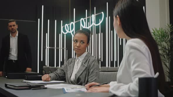 Man Comes to a Meeting with Female Colleagues in Modern Gray Office Room