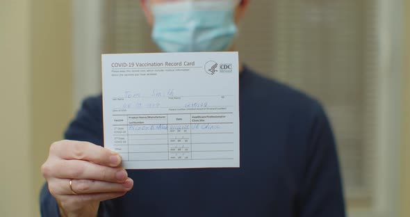 Man in Madical Mask Is Holding a Vaccination Record Card