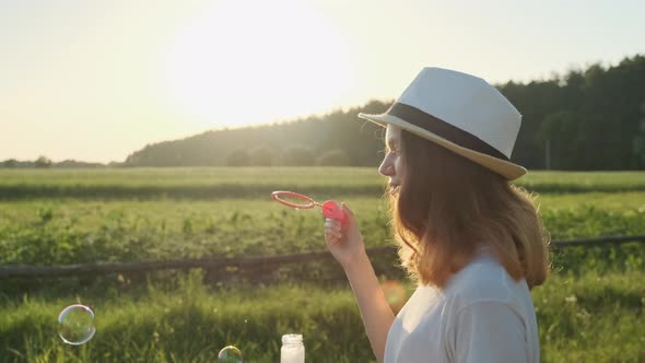 Beautiful Girl Teenager in a Hat Blowing Soap Bubbles