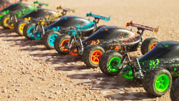 Multiple colourful remote-controlled buggy cars on start line in the desert.