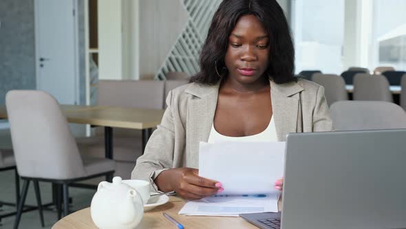 Black Businesswoman Drinks Tea Reading Papers in Cafe