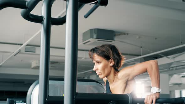 Young Woman is Doing Pushups on Uneven Bars in Gym