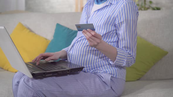 Unrecognizable Young Pregnant Woman Uses Laptop and Bank Card