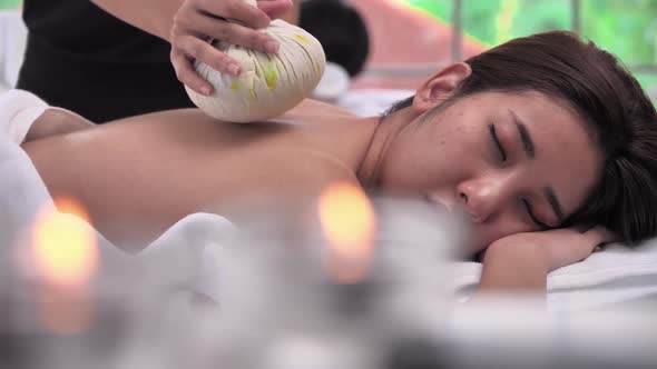 Young Asian woman getting relaxing during therapist put herbal spa ball on the back