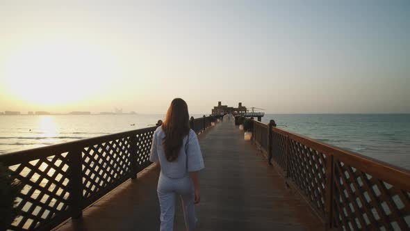 Woman Walking on Wooden Pier and Admiring Dubai Beach During Sunset