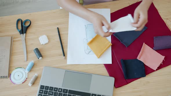 High Angle View of Modern Fashion Designer's Hands Choosing Farbic and Using Laptop at Table