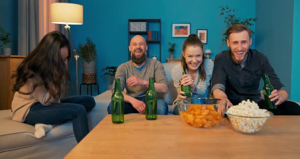 Friends Two Girls and Two Men Watching Series Movies Together on Couch Drinking Beer Laughing