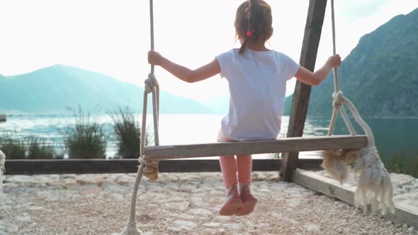 The Girl Swings on a Swing Near the Sea with a Beautiful View of the Bay and Mountains