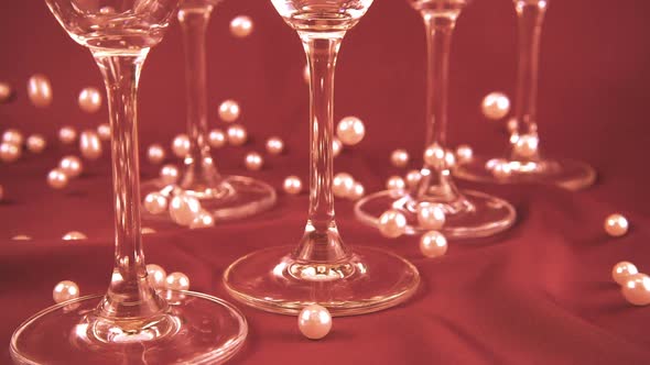 Falling white pearls next to wine glasses. Slow motion.