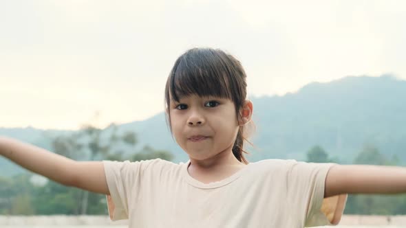 Cute Asian preschooler smiling happily and making heart-shaped hands on head on green nature