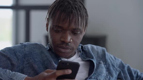 Closeup Portrait of Busy Thoughtful African American Man Texting on Smartphone Indoors