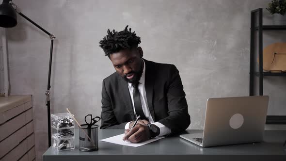 a Black Businessman in a Suit Makes Notes on a Sheet of Paper